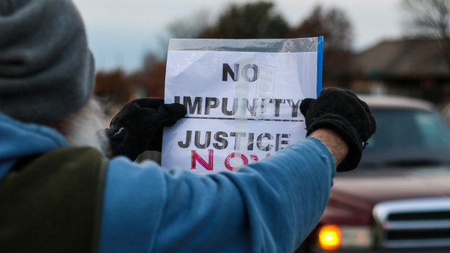 A protester holds a sign up in front of traffic that reads “no impunity justice now” at a vigil near 21st Street and Hillside on Nov. 30 in rememberance of the Ferguson, Mo. grand jury verdict. (Kevin Brown/The Sunflower)